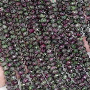 May include: A strand of green and pink gemstone beads. The beads are faceted and have a speckled appearance.