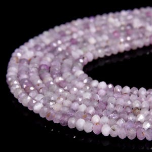 Peut inclure: Gros plan sur des brins de perles de pierres précieuses violet clair. Les perles sont facettées, captant la lumière pour créer un léger scintillement. La couleur varie du lavande au blanc. Les perles sont enfilées ensemble. Le fond est noir.
