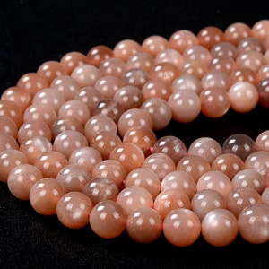 May include: A strand of round, smooth, peach-colored sunstone beads. The beads have a shimmery, iridescent quality.