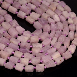 May include: A strand of pale lavender gemstone beads, each bead is a rectangular shape with rough edges, strung together with purple thread.