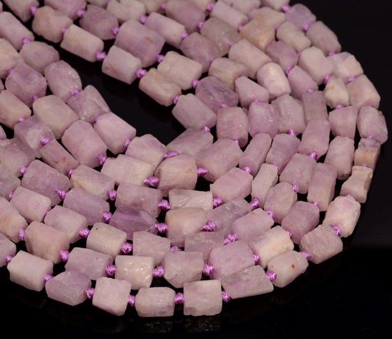 May include: A strand of pale lavender gemstone beads, each bead is a rectangular shape with rough edges, strung together with purple thread.