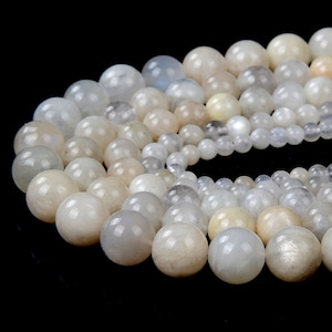 May include: A strand of white moonstone beads, with a variety of sizes and shapes. The beads are smooth and polished, with a subtle shimmer.