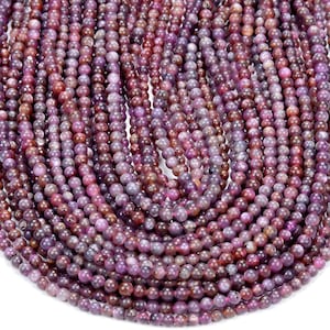 May include: A strand of round, purple and pink gemstone beads. The beads are smooth and have a slightly speckled appearance.