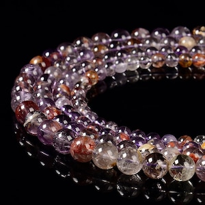 May include: A strand of purple and red gemstone beads. The beads are round and have a translucent appearance.