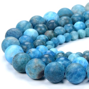 May include: A close-up of a collection of blue gemstone beads in various sizes. The beads range in color from light to dark blue, with a matte finish. The beads are round and appear to be strung together.