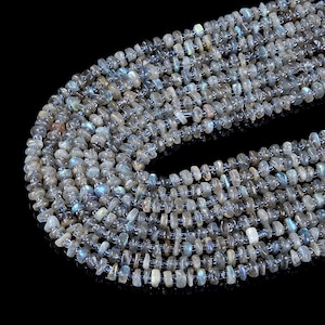 May include: Close-up of multiple strands of labradorite gemstone beads. The beads are a mix of gray, blue, and iridescent colors, with a slightly irregular shape. The beads are strung on a dark blue string, creating a textured and layered effect.