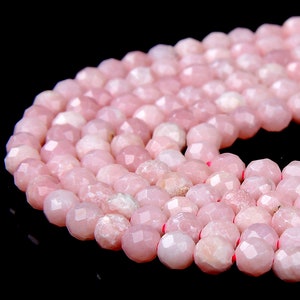 May include: A strand of pink gemstone beads with a faceted finish. The beads are round and have a light pink color.