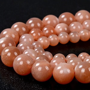May include: A strand of orange sunstone beads. The beads are round and have a smooth, polished finish.