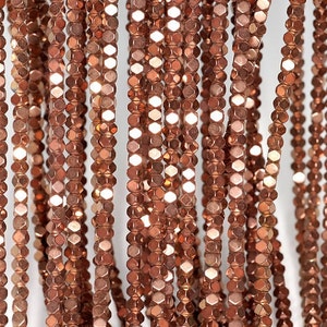 May include: A strand of copper-colored faceted beads. The beads are hexagonal in shape and have a metallic sheen.