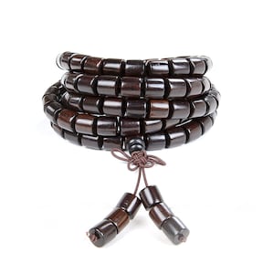Puede incluir: Un brazalete de cuentas de madera marrón oscuro con un borla anudada. El brazalete está hecho de cuentas redondas y está apilado en espiral.