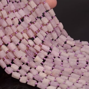 May include: A strand of light purple, faceted, square-shaped gemstone beads strung on a purple thread. The beads are approximately 6mm in size and have a rough, natural texture.