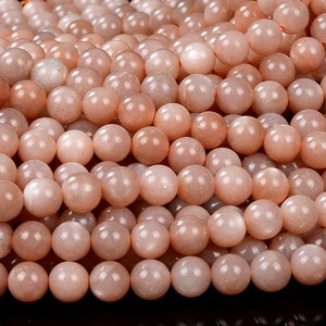 May include: A strand of peach-colored sunstone beads. The beads are round and have a smooth, polished finish.