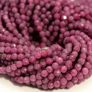 May include: A strand of pink ruby beads, each bead is faceted and has a slightly rough texture. The beads are strung together to form a long necklace or bracelet.