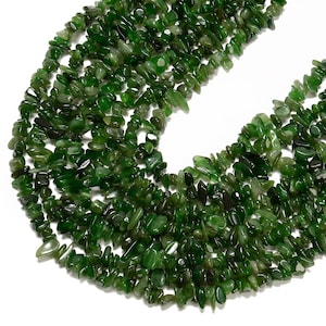 Könnte beinhalten: Eine Strähne grüner Jade-Chips. Die Perlen sind unregelmäßig geformt und haben eine natürliche, polierte Oberfläche.