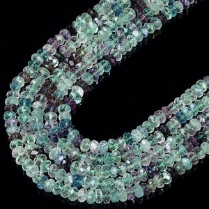 May include: A strand of faceted green, blue, and purple gemstone beads. The beads are faceted and have a slightly irregular shape. The beads are strung on a clear thread and are arranged in a loose, flowing pattern.
