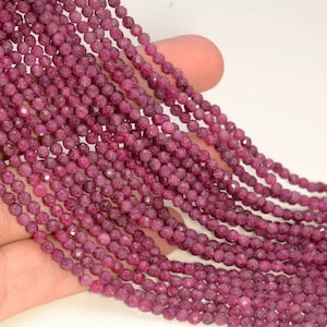 Könnte beinhalten: Eine Strähne aus rubinroten Edelsteinperlen, jede Perle ist facettiert und hat eine leicht unregelmäßige Form. Die Perlen sind auf einem durchsichtigen Faden aufgereiht und haben einen Durchmesser von etwa 4 mm.