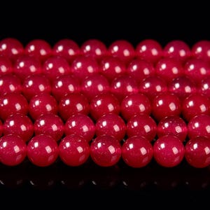 Peut inclure: Gros plan sur un brin de perles de pierres précieuses rouge vif. Les perles sont rondes et lisses, et elles sont disposées en rangée.