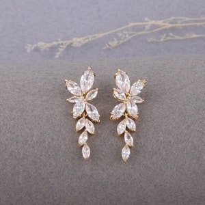 May include: A pair of gold dangle earrings with clear crystal stones in a floral design.