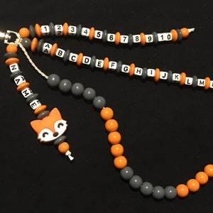 Könnte beinhalten: Eine graue und orangefarbene Perlenkette mit einem Fuchs-Anhänger. Die Kette hat Perlen mit den Buchstaben A bis P und den Zahlen 1 bis 10.