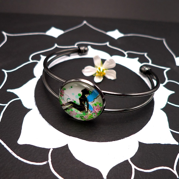 Bracelet jonc couleur gun metal avec cabochon en verre, fée aux ailes bleues assise au milieu des fleurs colorées dans la nature