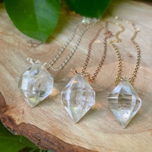 May include: Three diamond-shaped crystal pendants on necklaces with silver, copper, and gold chains. The crystals are clear and have a faceted design.