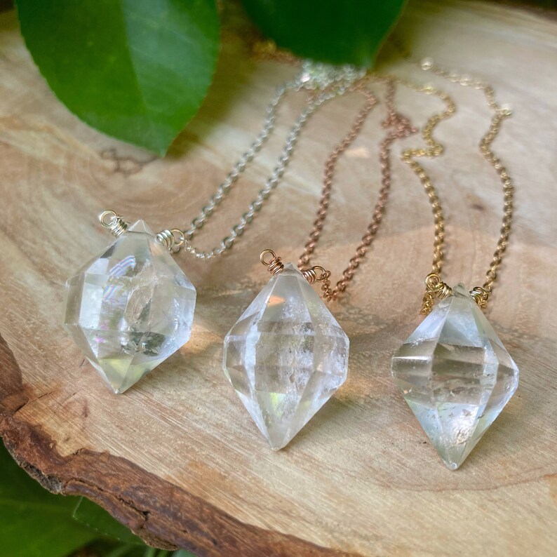 May include: Three diamond-shaped crystal pendants on necklaces with silver, copper, and gold chains. The crystals are clear and have a faceted design.