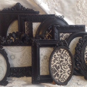May include: A set of nine black ornate picture frames with a decorative, damask-patterned paper insert. The frames are various sizes and shapes, including oval and square.