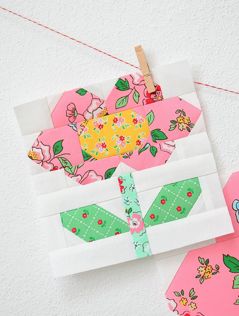 Pode incluir: Um bloco de tecido de flor rosa e verde com fundo branco. A flor &eacute; feita de v&aacute;rios quadrados de tecido menores e &eacute; cercada por uma borda branca.