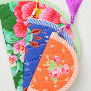 May include: Three semi-circular quilted pouches with zip closures. The largest is green with pink flowers, the middle is blue with a floral pattern, and the smallest is orange with pink roses. Each features a striped border and a colourful tassel.