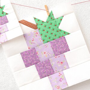 May include: A quilt block featuring a green star in the centre and a purple and white floral design in the background.