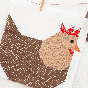 May include: A brown and white polka dot fabric square with a brown, white, and red fabric chicken applique. The chicken has a red comb and wattle, a black eye, and a small orange beak.