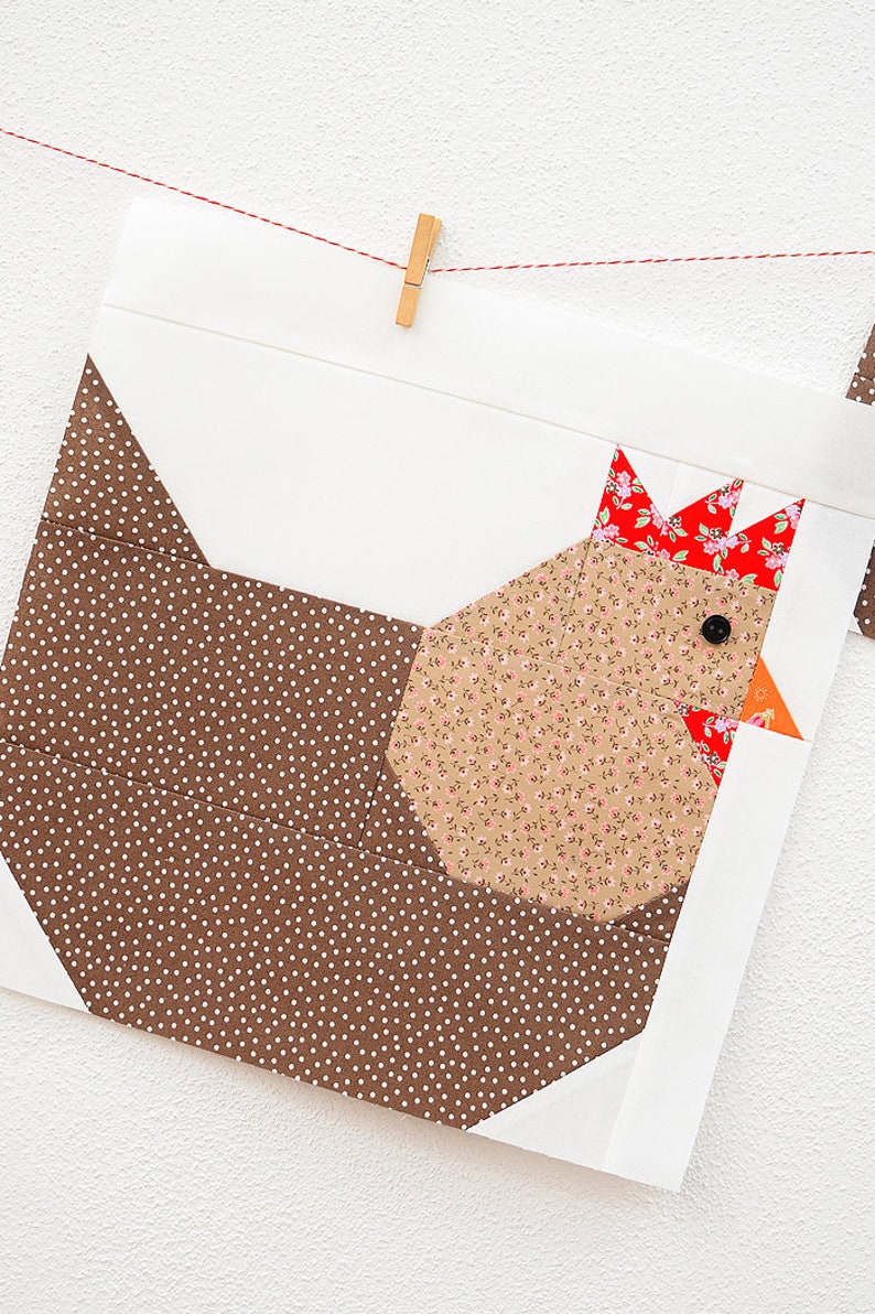 May include: A brown and white polka dot fabric square with a brown, white, and red fabric chicken applique. The chicken has a red comb and wattle, a black eye, and a small orange beak.
