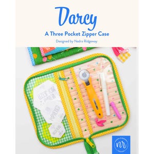 Könnte beinhalten: Ein Darcy Drei-Taschen-Reißverschlussetui, entworfen von Nadra Ridgeway. Das offene Stoffetui hat eine grün karierte Tasche, eine durchsichtige Vinyltasche mit einem gelben Rollschneider, einem weißen Stift und einem rosa Werkzeug sowie Papier-Sechsecke.
