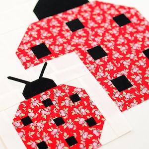 K&ouml;nnte beinhalten: Zwei rote und schwarze Marienk&auml;fer-Patchworkbl&ouml;cke mit einem Blumenmuster. Der gr&ouml;&szlig;ere Marienk&auml;fer liegt auf dem kleineren.