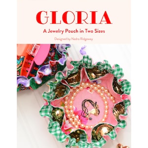 May include: A jewelry pouch in two sizes, with the name "GLORIA" in red. The pouch is pink with a floral pattern and a green and white checkered trim. The pouch contains jewelry, including necklaces and pearls.