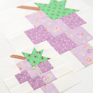 May include: A quilt block featuring a green star and squares of purple floral fabric. The block is made with a white background and brown fabric strips.