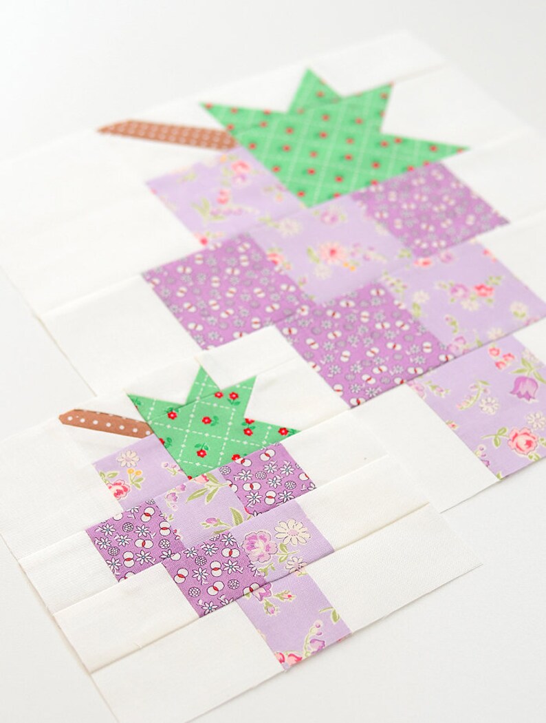 May include: A quilt block featuring a green star and squares of purple floral fabric. The block is made with a white background and brown fabric strips.