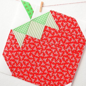 Peut inclure: Un bloc de courtepointe en tissu rouge en forme de fraise. Le bloc est compos&eacute; de petits carr&eacute;s de tissu rouge, vert et blanc. Le tissu rouge a un petit motif floral.