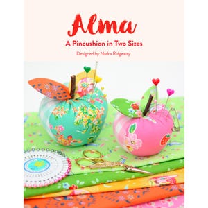 May include: Two apple-shaped pincushions with fabric leaves and stems, one green and one pink, are displayed. The pincushions are filled with pins and needles. The image also shows scissors, fabric, and the text "Alma, A Pincushion in Two Sizes."
