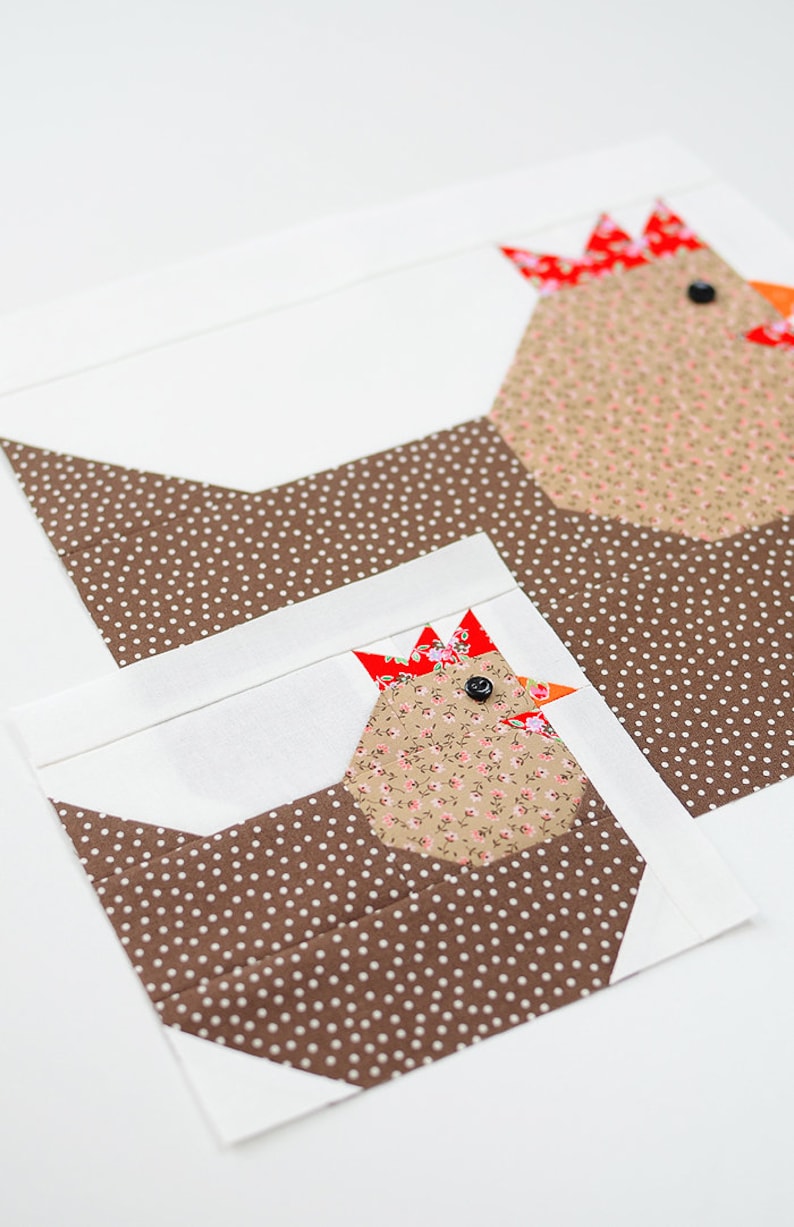May include: Two brown and white fabric chickens with red and white combs and black eyes. The chickens are sewn together and have a white background.