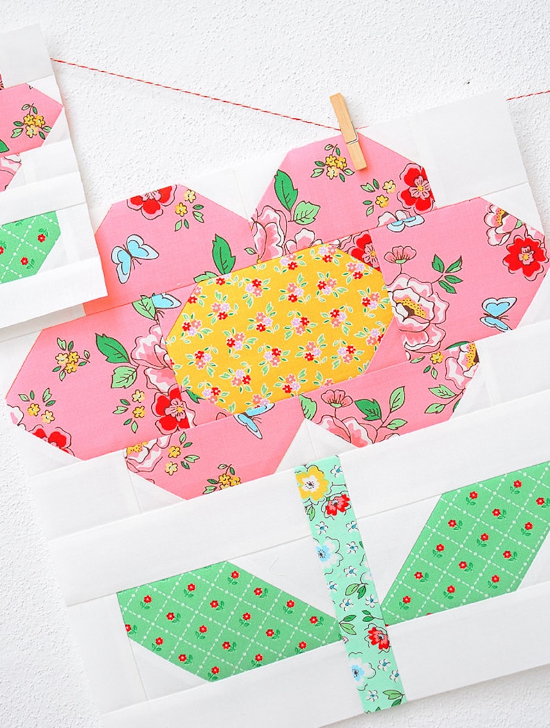 Pode incluir: Uma flor de tecido floral rosa e amarelo com folhas verdes sobre um fundo branco. A flor &eacute; feita de v&aacute;rias pe&ccedil;as de tecido costuradas juntas.