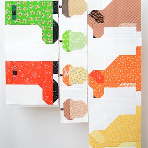 May include: A set of fabric quilt blocks featuring a whimsical acorn design. The blocks are made with a variety of colourful fabrics, including green, orange, yellow, and brown. The blocks are arranged in a vertical row, with the acorn design repeated in each block.