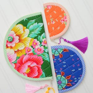 May include: Three semi-circular quilted pouches with zip closures and colourful tassels. One large green pouch features a floral pattern, a medium blue pouch has a geometric floral print, and a small orange pouch displays a rose pattern.