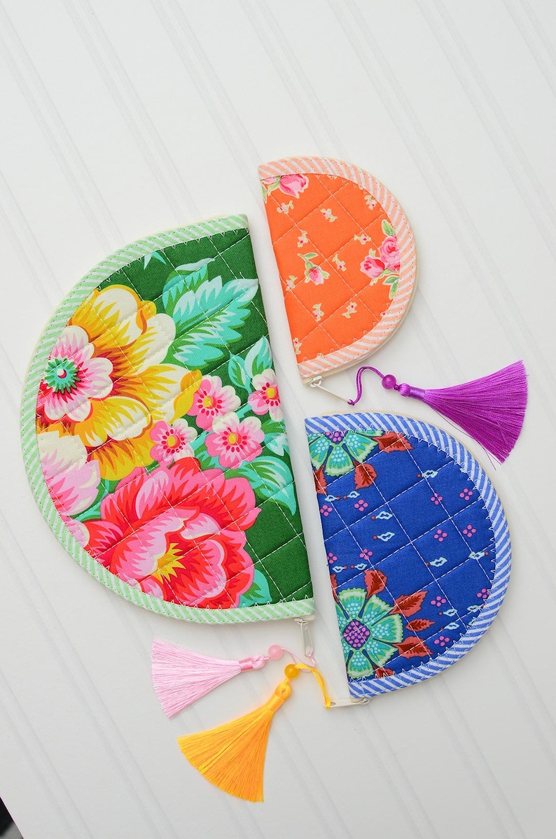 May include: Three semi-circular quilted pouches with zip closures and colourful tassels. One large green pouch features a floral pattern, a medium blue pouch has a geometric floral print, and a small orange pouch displays a rose pattern.
