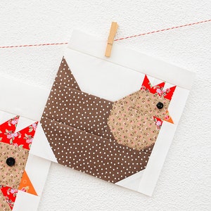 May include: A brown and white polka dot fabric chicken applique with a floral print body and red and white floral print comb. The applique is hanging from a red string with a wooden clothespin.