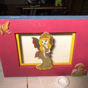 Wooden coin bank with a fairy, a butterfly, and a mushroom.