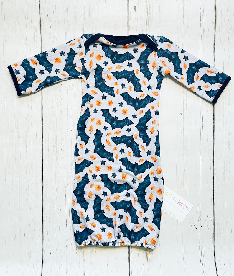 Puede incluir: Un camis&oacute;n de beb&eacute; con un estampado azul marino, blanco y naranja. El estampado presenta murci&eacute;lagos, estrellas y hojas. El camis&oacute;n tiene mangas largas con ribete azul marino y un escote azul marino. El camis&oacute;n est&aacute; hecho de tela suave.