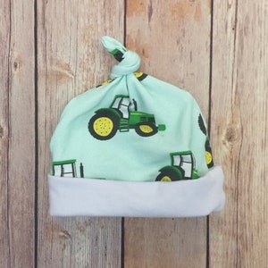 May include: A light blue baby hat with a white brim. The hat has a knot on top and a tractor print.