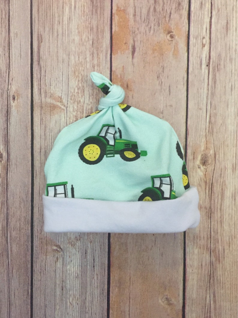 May include: A light blue baby hat with a white brim. The hat has a knot on top and a tractor print.