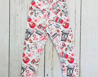 May include: White leggings with a red and black print of coffee cups, candy canes, and snowflakes. The leggings have the text "Peppermint Mocha" and "Coffee Time" on them. The leggings are made by Jake 'n beth.